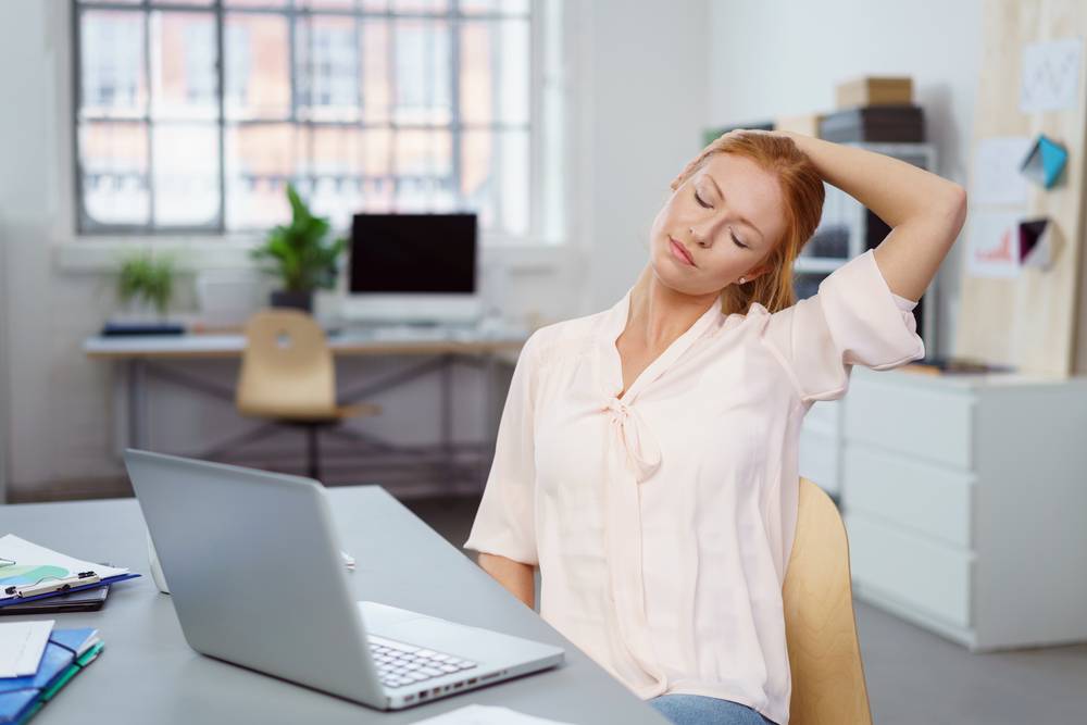 A woman stretches in front of her computer to relax tense neck muscles.