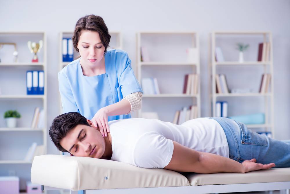 A physiotherapist providing neck pain treatment as the man lies on the treatment table.